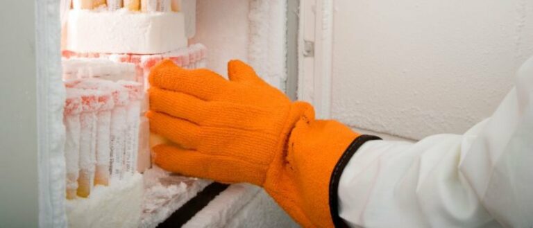 an orange gloves hand reaches into a biobank freezer to work with samples