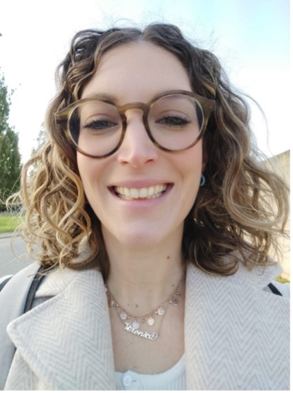 A white woman with curly blonde hair who wears glasses is smiling at the camera