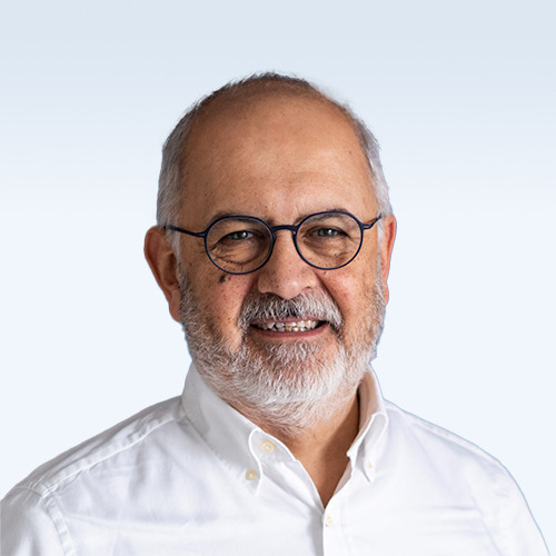 The image of a man wearing a white shirt and glasses. He is smiling at the camera in front of a neutral background.