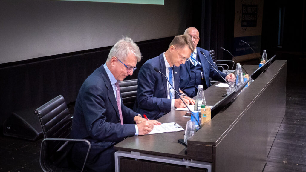 The picture of 3 men sitting and signing papers.